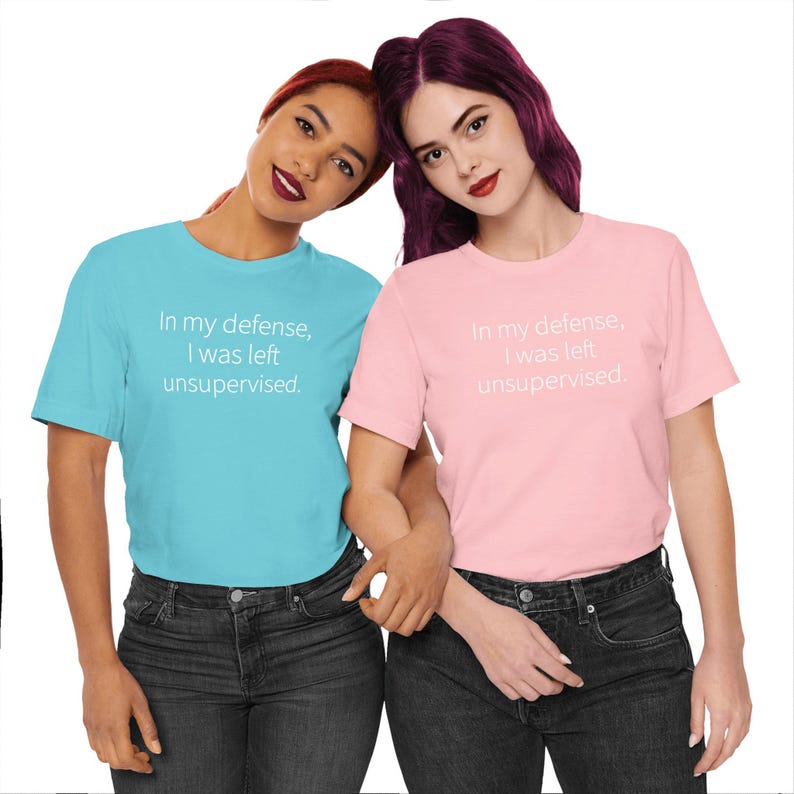 Peut inclure: Deux femmes portant des t-shirts assortis. L'un est bleu clair, l'autre rose. Les deux chemises portent l'inscription "In my defense, I was left unsupervised" en blanc. Elles portent toutes les deux des jeans d&eacute;lav&eacute;s fonc&eacute;s.