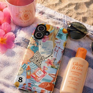 May include: A beach scene featuring a phone case, sunglasses, and sunscreen. The phone case has a collage design with the text "how lucky are we". A pink cup with "SUNSHINE IN A CUP" is nearby. The sunscreen bottle reads "Glow & Go".