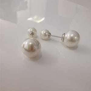 May include: A pair of double-sided pearl earrings. Each earring has a small pearl stud and a larger, lustrous pearl drop. The earrings are connected by a silver post, creating a sophisticated and timeless accessory.