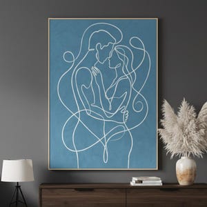 Puede incluir: Una impresión enmarcada que representa un dibujo de línea continua de una pareja abrazándose. La obra de arte utiliza líneas blancas sobre un fondo azul. El marco es de color madera clara. La obra de arte se exhibe en un mueble de madera marrón oscuro.