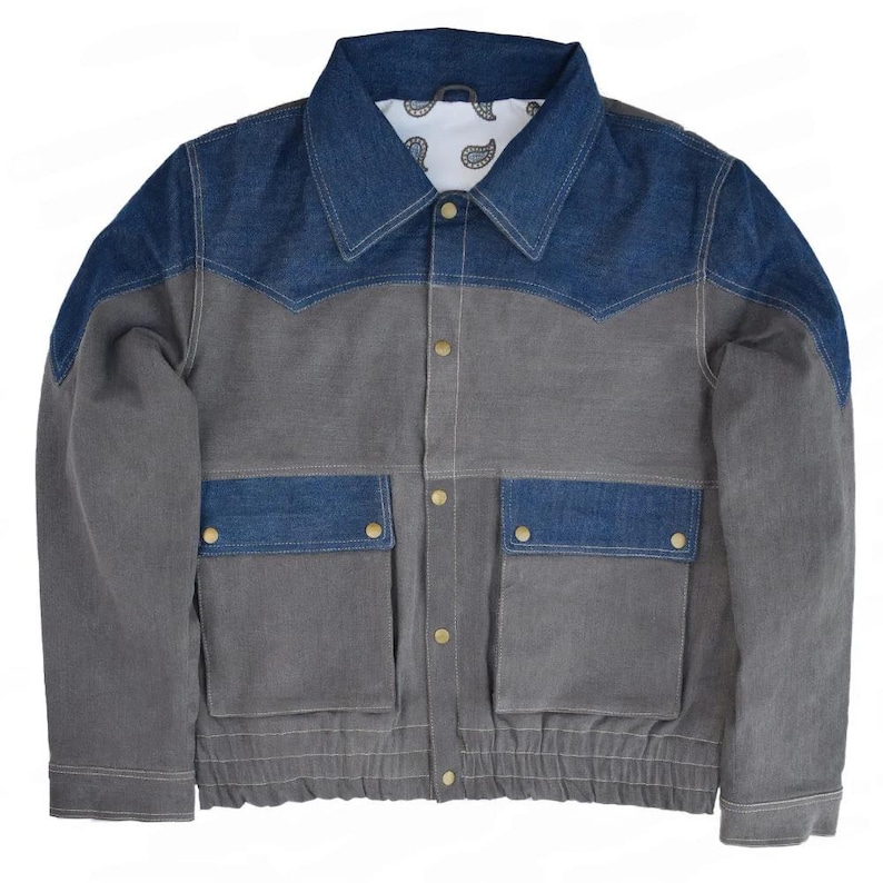 May include: A gray and blue denim jacket with a classic design. The jacket features a blue denim collar and shoulder yoke, two front pockets, and gold-colored buttons. The interior lining has a white paisley pattern.