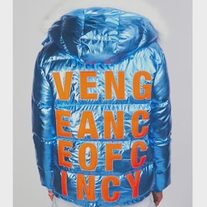 May include: A shiny, blue puffer jacket with a hood and white faux fur trim. The back of the jacket features the orange text "VENGEANCE OF INCY". The jacket is a vibrant, eye-catching piece.