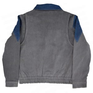 May include: A gray jacket with a denim collar and denim shoulder accents. The jacket has a ribbed hem and cuffs, and a zipper closure. The back of the jacket is visible in the image.