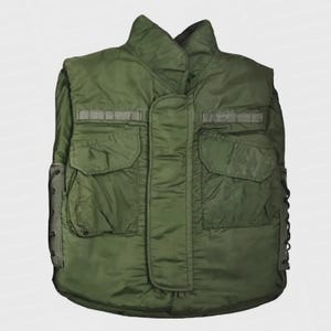 May include: An olive green military-style vest with a high collar and multiple pockets. The vest has a quilted appearance and features reinforced sections and adjustable side straps. The design suggests a focus on durability and functionality, typical of military apparel.