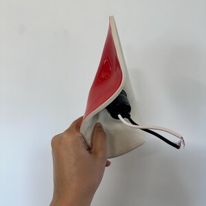 May include: A curved, cone-shaped lamp shade with a glossy red exterior and a matte white interior. A black plastic light socket is attached to the center, featuring two exposed electrical wires, one black and one white, extending from the base.