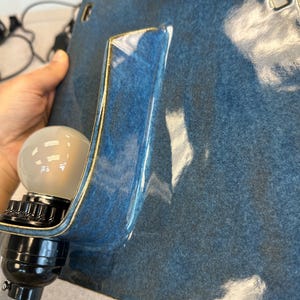 May include: A blue ceramic wall sconce with a glossy finish and a gold trim. The sconce has a rectangular shape with a curved section to hold a light bulb. The light bulb is a standard size and shape.