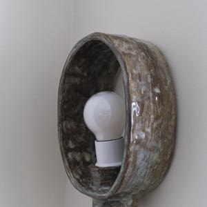 May include: A ceramic wall sconce with a bulb. The sconce has a brown and blue-green mottled glaze. The light bulb is white. The sconce is mounted on a white wall. The fixture is a decorative lighting element.