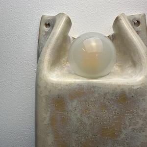 May include: A wall-mounted ceramic light fitting featuring a glossy, cream-coloured glaze with a crackled texture and golden-brown crystalline patterns. The fitting has a sculptural, organic shape with two mounting holes and a central frosted glass globe.
