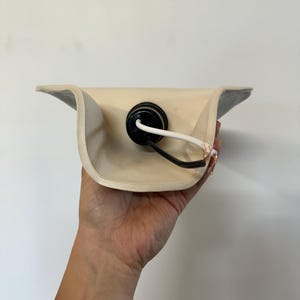 May include: A cream-colored curved ceramic lamp shade featuring a central black socket housing. A white electrical cord with exposed copper wiring extends from the socket, which is mounted in the center of the concave interior of the shade.