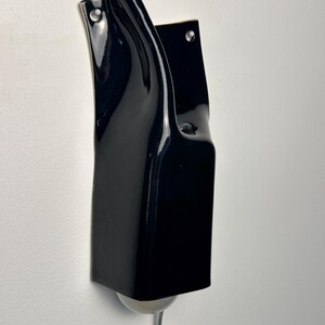 May include: A wall-mounted lamp featuring a glossy, dark navy blue ceramic fixture with a curved, organic silhouette. The structure includes two visible mounting holes at the top and a small, round, white light bulb protruding from the bottom.