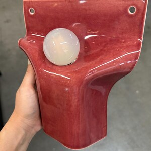 Pode incluir: Um candeeiro de parede em cer&acirc;mica com um acabamento brilhante em rosa profundo e uma forma org&acirc;nica ondulada. A pe&ccedil;a inclui dois orif&iacute;cios de montagem circulares no topo e uma l&acirc;mpada esf&eacute;rica &uacute;nica em vidro branco fosco.