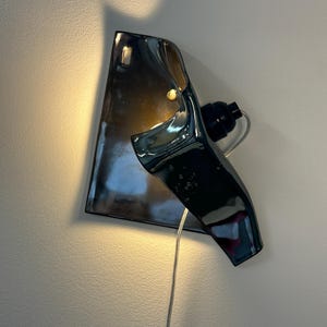 Peut inclure: Une applique murale compos&eacute;e d'un abat-jour en c&eacute;ramique gris anthracite brillant &agrave; la forme irr&eacute;guli&egrave;re et repli&eacute;e. Le luminaire comprend une douille noire et un cordon d'alimentation transparent, diffusant une lueur chaude et douce.