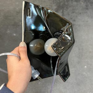 Peut inclure: Une applique murale compos&eacute;e d'un abat-jour en c&eacute;ramique noir brillant &agrave; la silhouette irr&eacute;guli&egrave;re et pli&eacute;e. Le luminaire comprend une ampoule blanche, une douille noire et un cordon &eacute;lectrique transparent avec une fiche &agrave; deux broches.