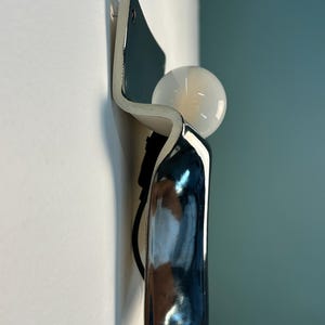Peut inclure: Une applique murale compos&eacute;e d'un corps incurv&eacute; en c&eacute;ramique ou en m&eacute;tal bleu fonc&eacute; brillant avec une finition lisse et r&eacute;fl&eacute;chissante. Une ampoule sph&eacute;rique en verre blanc est plac&eacute;e dans la courbe sup&eacute;rieure du luminaire, vers l'ext&eacute;rieur.