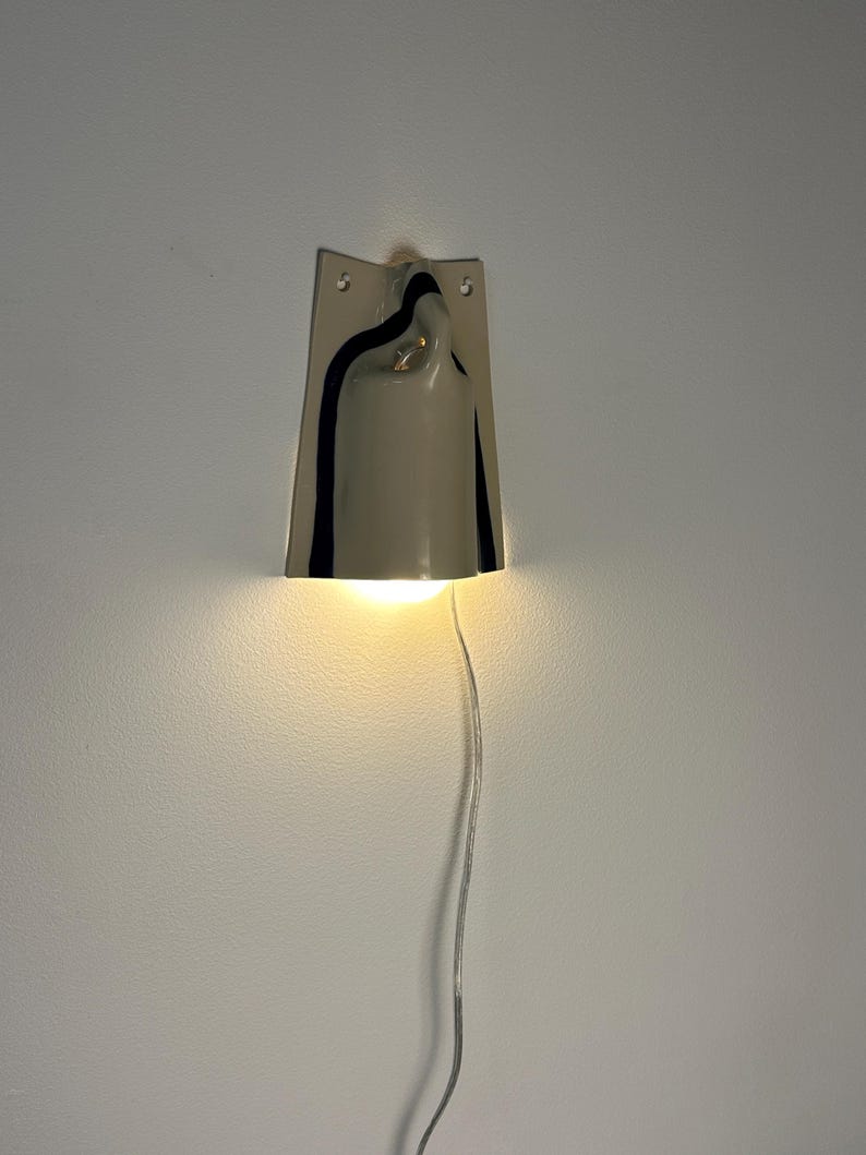 May include: A wall-mounted light fixture featuring a glossy, light gray ceramic shade with a curved, bell-like silhouette. The shade is accented by dark, vertical black stripes along the sides and emits a warm, downward-facing glow.