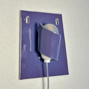 Pode incluir: Arandela de parede moderna com base de cer&acirc;mica roxa e abajur curvo na cor lavanda. A arandela apresenta uma l&acirc;mpada branca e um cabo de alimenta&ccedil;&atilde;o transparente. Design minimalista e contempor&acirc;neo, adequado para ilumina&ccedil;&atilde;o interior.