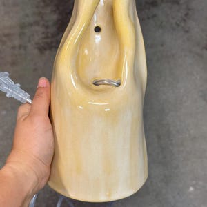 Pu&ograve; includere: Un'applique da parete in ceramica giallo pallido con finitura liscia e lucida e una forma organica e fluida. Il corpo illuminante presenta un foro di montaggio circolare nella parte superiore e un'apertura centrale per il cavo elettrico.