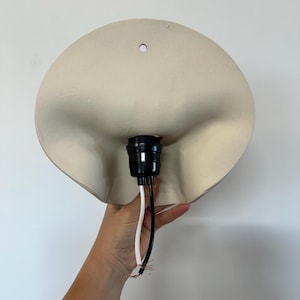 May include: A matte off-white wall lamp fixture with a curved, organic shape and a single mounting hole at the top. The center features a black plastic light socket assembly with one white wire and one black wire extending from the base.