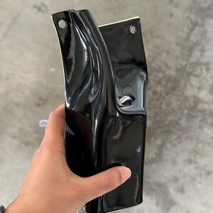 May include: A glossy black ceramic wall planter with a curved, organic shape. The piece features two circular holes at the top for mounting and a central opening with a silver metal ring detail, showcasing a smooth, reflective finish throughout.
