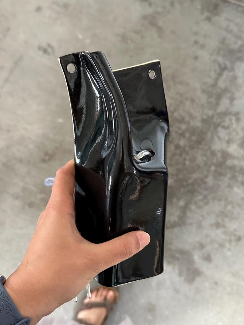 May include: A glossy black ceramic wall planter with a curved, organic shape. The piece features two circular holes at the top for mounting and a central opening with a silver metal ring detail, showcasing a smooth, reflective finish throughout.