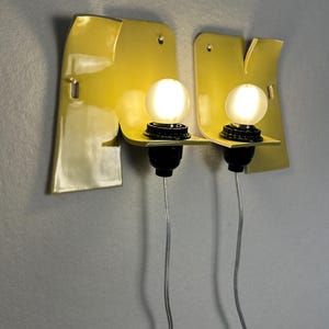 May include: Two wall-mounted light fixtures featuring glossy yellow ceramic backplates with irregular, organic shapes. Each fixture includes a black socket holding a round, frosted white light bulb, with a thin, clear electrical cord extending downward.