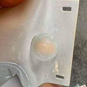 May include: A white ceramic wall plate featuring a central circular opening with a translucent, milky glass dome insert. The rectangular plate has two small, rectangular slots positioned vertically near the top and bottom edges of the surface.