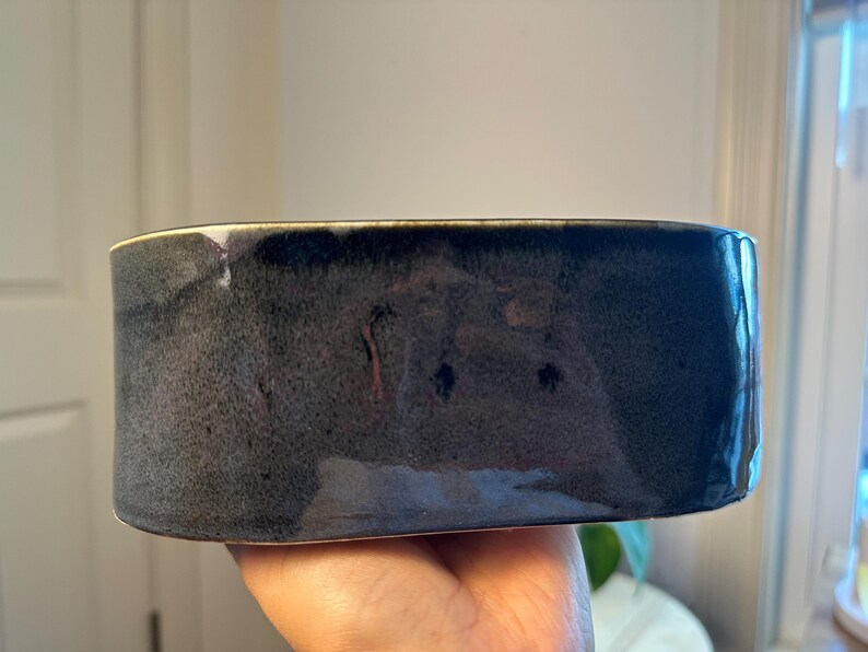 May include: A rectangular ceramic container with a dark blue and grey glaze. The handmade pottery piece has a glossy finish and is held in a person's hand. The container is approximately 15 cm long.