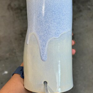 K&ouml;nnte beinhalten: Ein zylindrischer Lampenfu&szlig; aus Keramik mit zweifarbiger Glasur. Der obere Teil hat eine gesprenkelte hellblaue Oberfl&auml;che, die &uuml;ber einen glatten, cremewei&szlig;en unteren Bereich verl&auml;uft. Ein transparentes Stromkabel f&uuml;hrt durch ein Loch im Fu&szlig;.