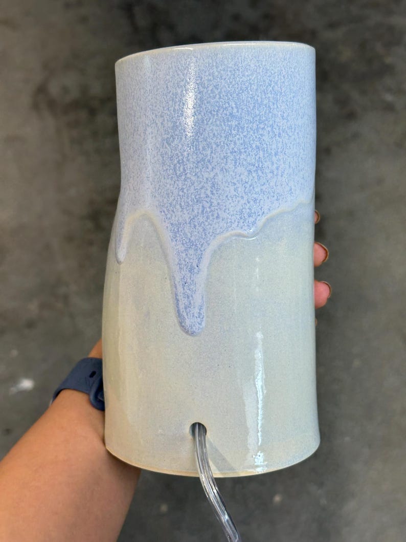 K&ouml;nnte beinhalten: Ein zylindrischer Lampenfu&szlig; aus Keramik mit zweifarbiger Glasur. Der obere Teil hat eine gesprenkelte hellblaue Oberfl&auml;che, die &uuml;ber einen glatten, cremewei&szlig;en unteren Bereich verl&auml;uft. Ein transparentes Stromkabel f&uuml;hrt durch ein Loch im Fu&szlig;.