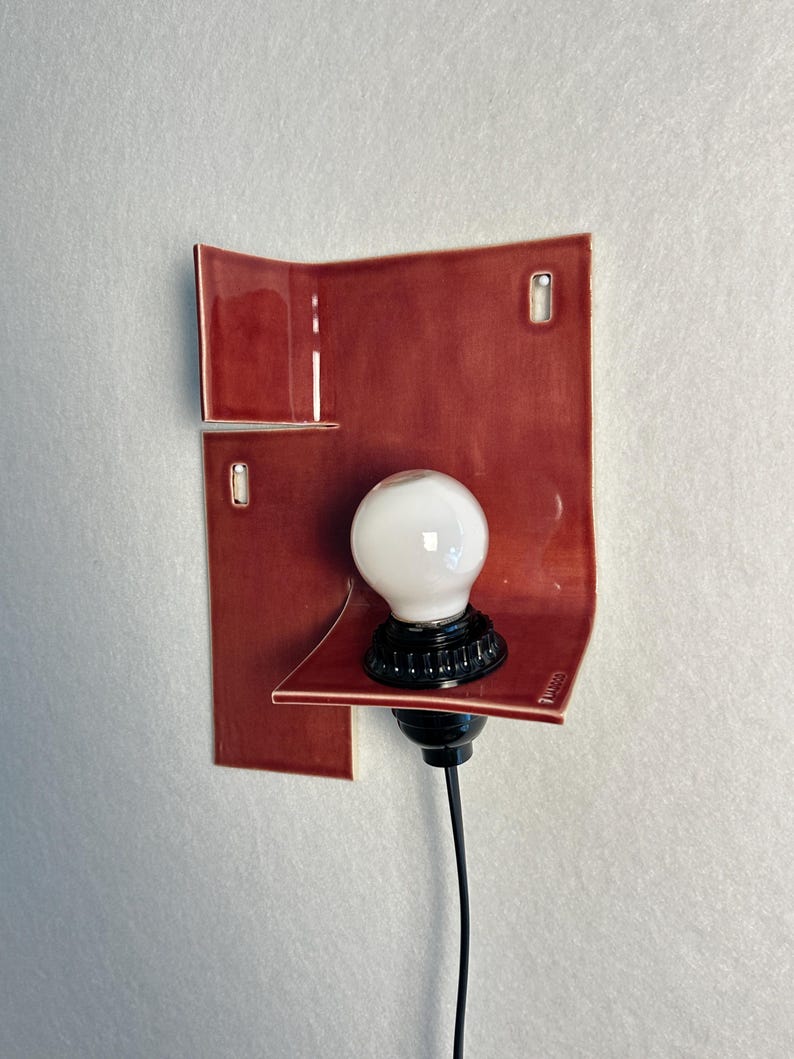 Pode incluir: Arandela de parede moderna com abajur de cer&acirc;mica vermelha e l&acirc;mpada branca. A base e o cabo s&atilde;o pretos. O design &eacute; minimalista e contempor&acirc;neo.