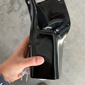 May include: A glossy black ceramic wall sconce with a curved, elongated silhouette. The fixture features two circular mounting holes at the top and a central opening designed to hold a light bulb, with a clear electrical cord extending from the base.