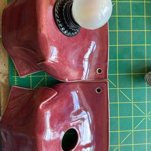 Puede incluir: Dos apliques de pared cuadrados de cer&aacute;mica en color rojo intenso brillante con bordes ondulados y plegados. Cada aplique tiene una abertura circular central para una bombilla y dos peque&ntilde;os orificios de montaje. Uno tiene una bombilla blanca.