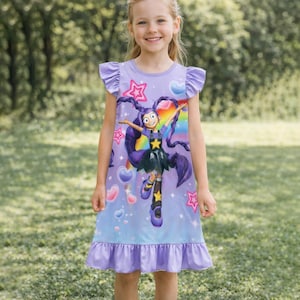 Könnte beinhalten: Ein helllila Kleid mit einem Cartoon-Charakter-Aufdruck. Das Kleid hat einen Rüschensaum und Ärmel. Die Cartoonfigur hat lila Haare und ist vor einem Hintergrund aus Sternen, Herzen und einem Regenbogen abgebildet.