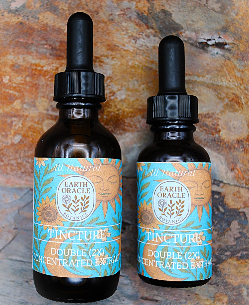 Op de afbeelding: Twee donker amberkleurige tinctuurflessen met zwarte druppelaars. De etiketten hebben een turquoise achtergrond met een zon- en zonnebloemontwerp en de tekst "Earth Oracle Botanics Tincture Double (2X) Concentrated Extract."