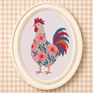 Può includere: Un ricamo a punto croce raffigurante un gallo all'interno di una cornice ovale color crema. Il gallo presenta un corpo grigio chiaro decorato con fiori rosa e foglie verde ottanio scuro, una cresta e bargigli rossi e una coda con piume rosse, arancioni e verde ottanio.