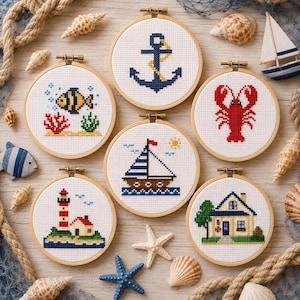 May include: Six circular wooden embroidery hoops containing cross-stitch designs with nautical themes, including an anchor, a fish, a lobster, a sailboat, a lighthouse, and a house, arranged with seashells, a toy boat, and rope.