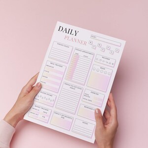 May include: A daily planner with a soft pink and yellow gradient design. The planner includes sections for goals, appointments, meal tracking, water intake, and notes. The text "DAILY PLANNER" is at the top.