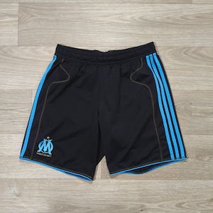 May include: Black athletic shorts with three light blue stripes down the side and light blue trim. The shorts feature the logo of a sports team in light blue. The shorts are made of a breathable material.