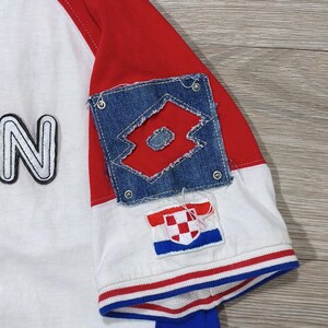 May include: White and red baseball style shirt with blue accents. The shirt features a denim patch with a red logo and a Croatian flag patch. The sleeve is red, and the shirt has a blue stripe on the bottom.