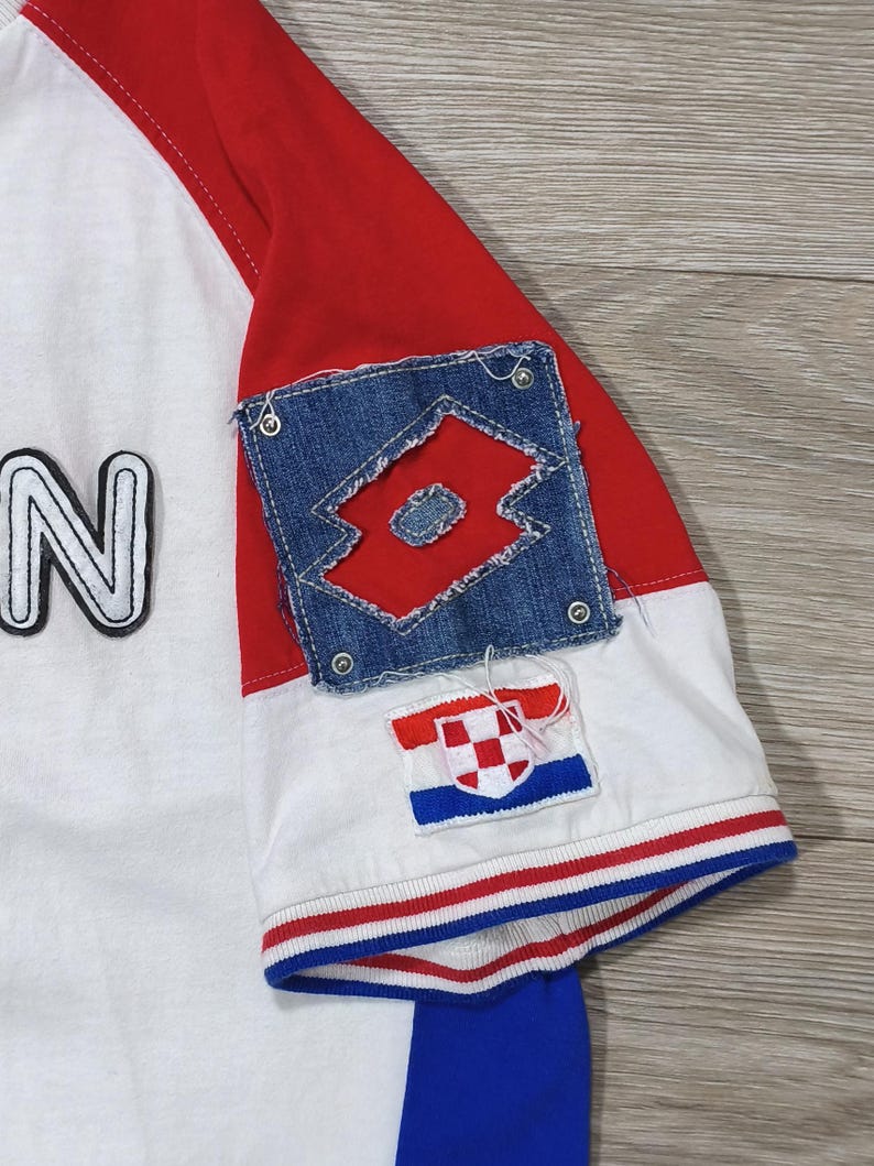 May include: White and red baseball style shirt with blue accents. The shirt features a denim patch with a red logo and a Croatian flag patch. The sleeve is red, and the shirt has a blue stripe on the bottom.