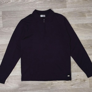 Peut inclure: Un haut à manches longues de couleur violet foncé doté d'un col et d'une fermeture éclair sur le quart supérieur. Le vêtement présente un ourlet droit et une petite étiquette métallique rectangulaire de marque sur le bas à droite.