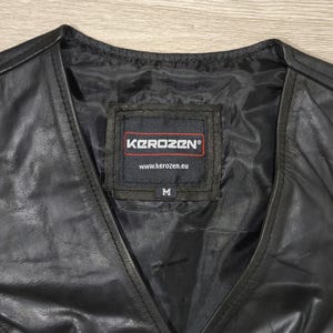 May include: Black leather vest with a V-neck design. The vest features a label with the brand name "Kerozen" and the size "M". The vest is made of a shiny, smooth material.