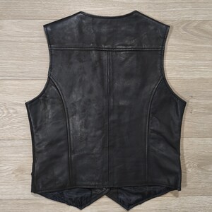 May include: A black leather vest with a classic design. The vest features a V-neck, a tailored fit, and a smooth, shiny finish. The back of the vest is visible, showcasing the stitching and panel details. The vest is likely made of genuine leather.