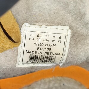 May include: A close-up of a white label with black text, including size conversions: UK 5 1/2, USA M 6, EUR 39, USA W 7 1/2. The label also states "MADE IN VIETNAM".