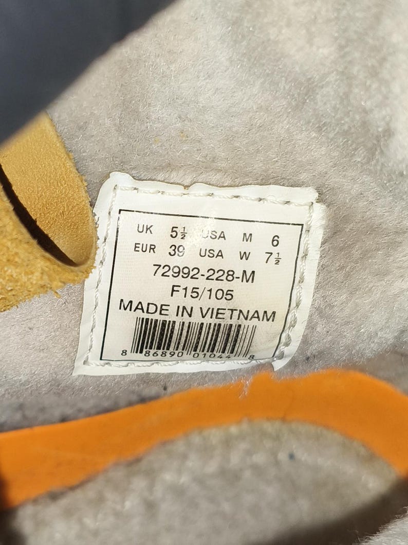 May include: A close-up of a white label with black text, including size conversions: UK 5 1/2, USA M 6, EUR 39, USA W 7 1/2. The label also states "MADE IN VIETNAM".