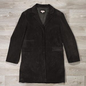 Peut inclure: Un manteau en daim marron foncé doté d'un revers cranté, de manches longues et de deux poches à rabat sur le devant. L'intérieur est doublé d'un tissu sombre et comporte une étiquette au niveau du col avec le texte AX.
