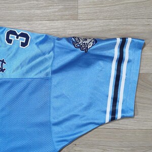 May include: Light blue jersey with the number 3 in navy blue on the shoulder. The sleeve has navy and white stripes. A logo is visible on the shoulder. The jersey is made of a breathable, mesh-like fabric.