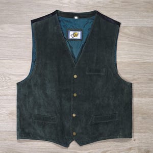Pode incluir: Colete de camurça verde escuro com decote em V, quatro botões dourados e dois bolsos frontais. O colete tem forro azul-petróleo e uma pequena etiqueta com um logotipo. Estilo clássico.
