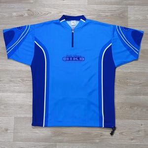 May include: A bright blue short-sleeve cycling jersey with a quarter-zip collar, dark blue side panels, and white piping accents. The chest features the text Full Time BIKE in a dark blue oval graphic. The hem includes a black adjustable cord.