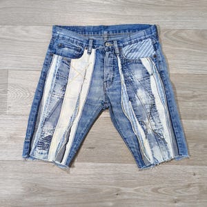 Peut inclure: Short en jean bleu avec des rayures verticales blanches et bleu clair. Le short a une fermeture boutonnée, des poches avant et un ourlet effiloché. Le design présente un style patchwork avec des détails usés.
